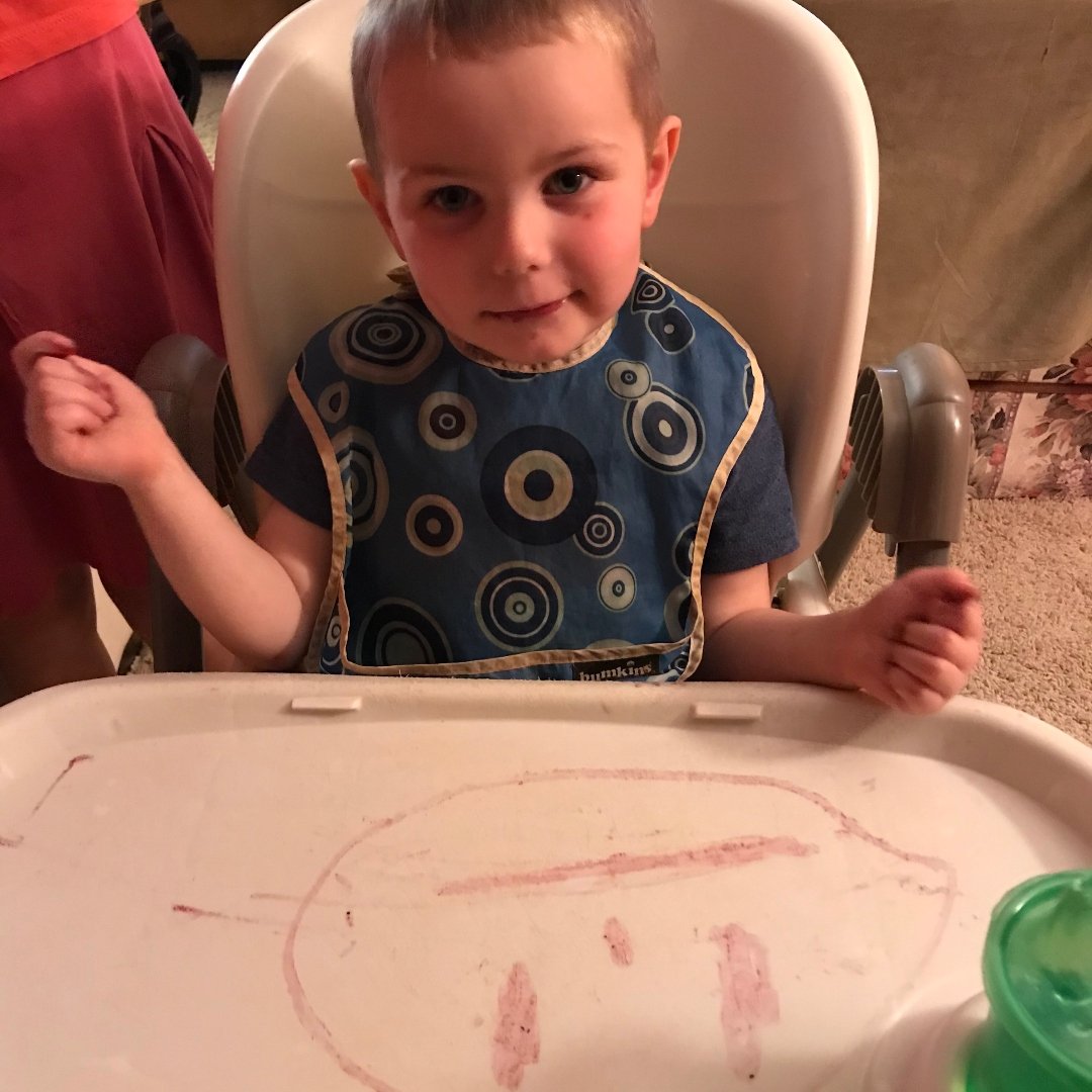 little boy with smiley face drawn on high chair tray