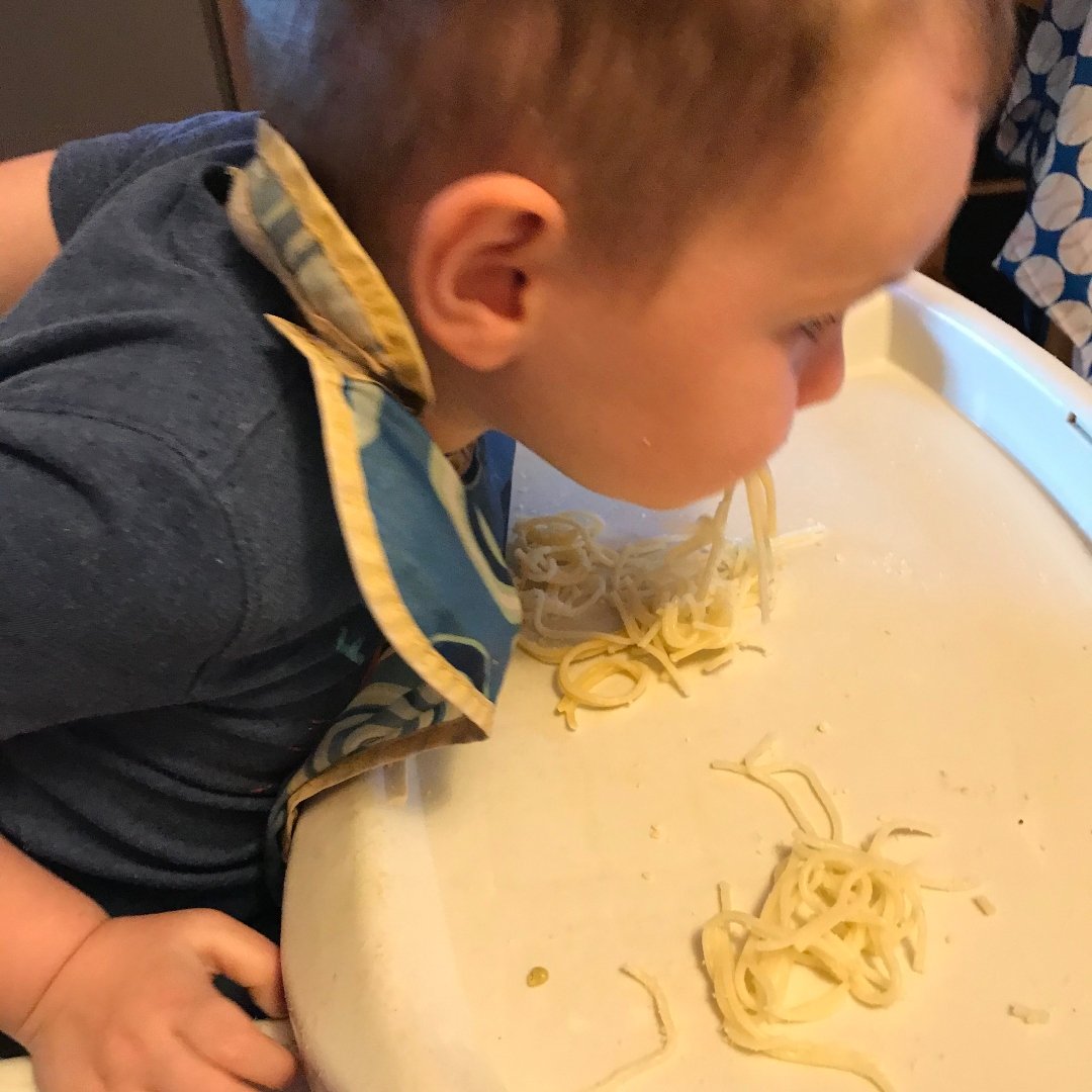 little boy slurping spaghetti off high chair tray