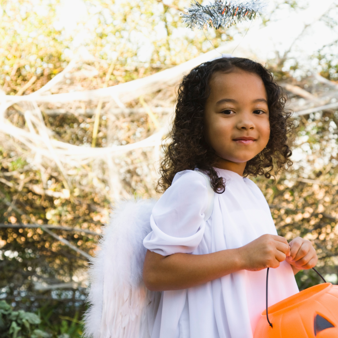 little girl dressed as an angel and carrying a pumpkin