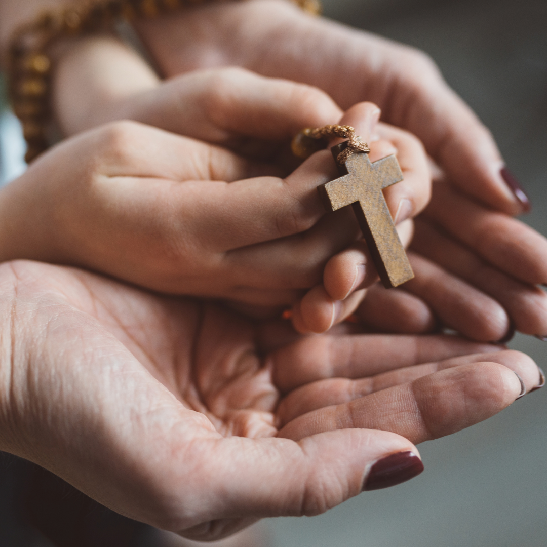mom and child holding a wooden rosary, close-up of hands only