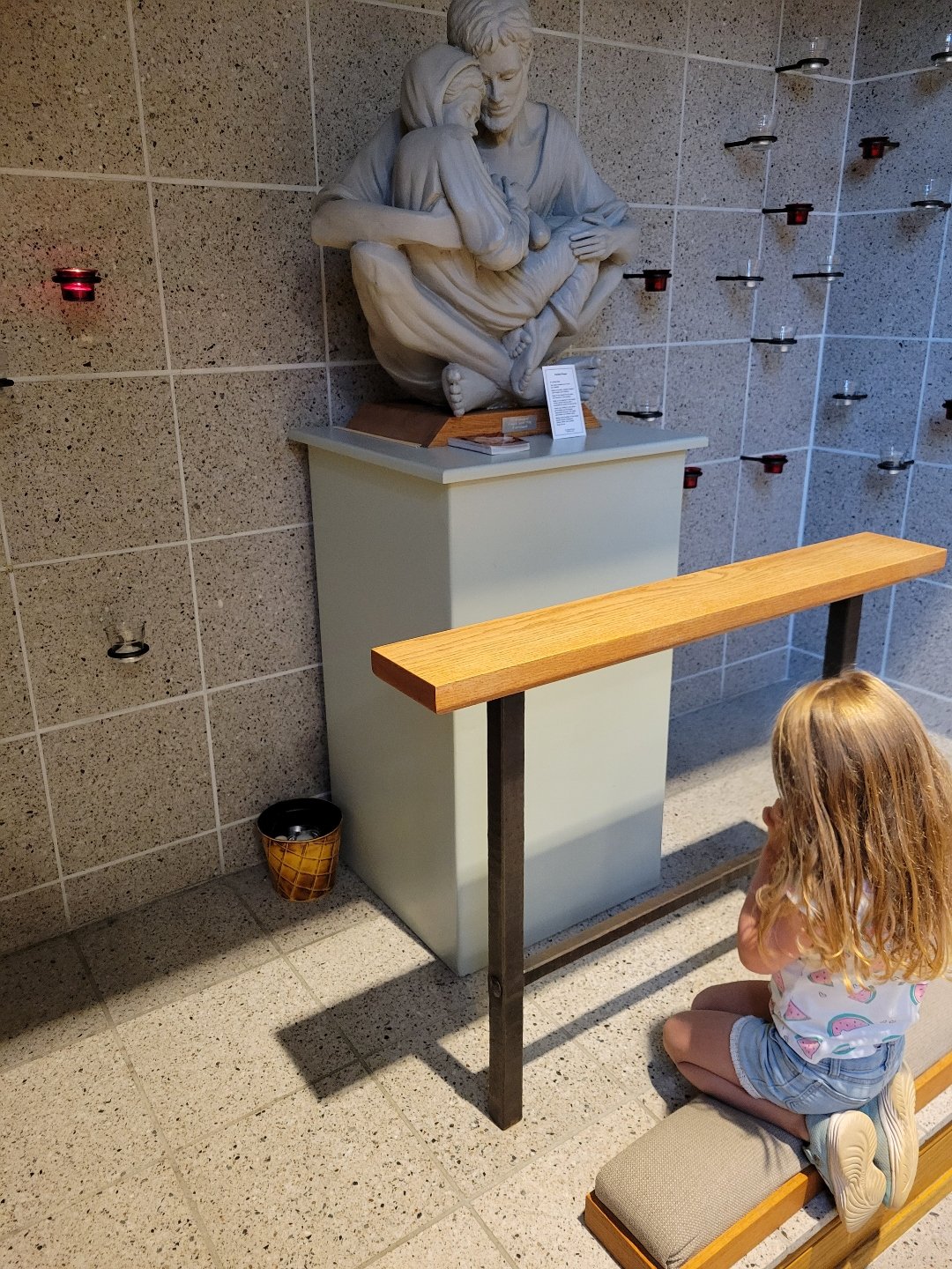 little girl praying in front of Holy Family sculpture