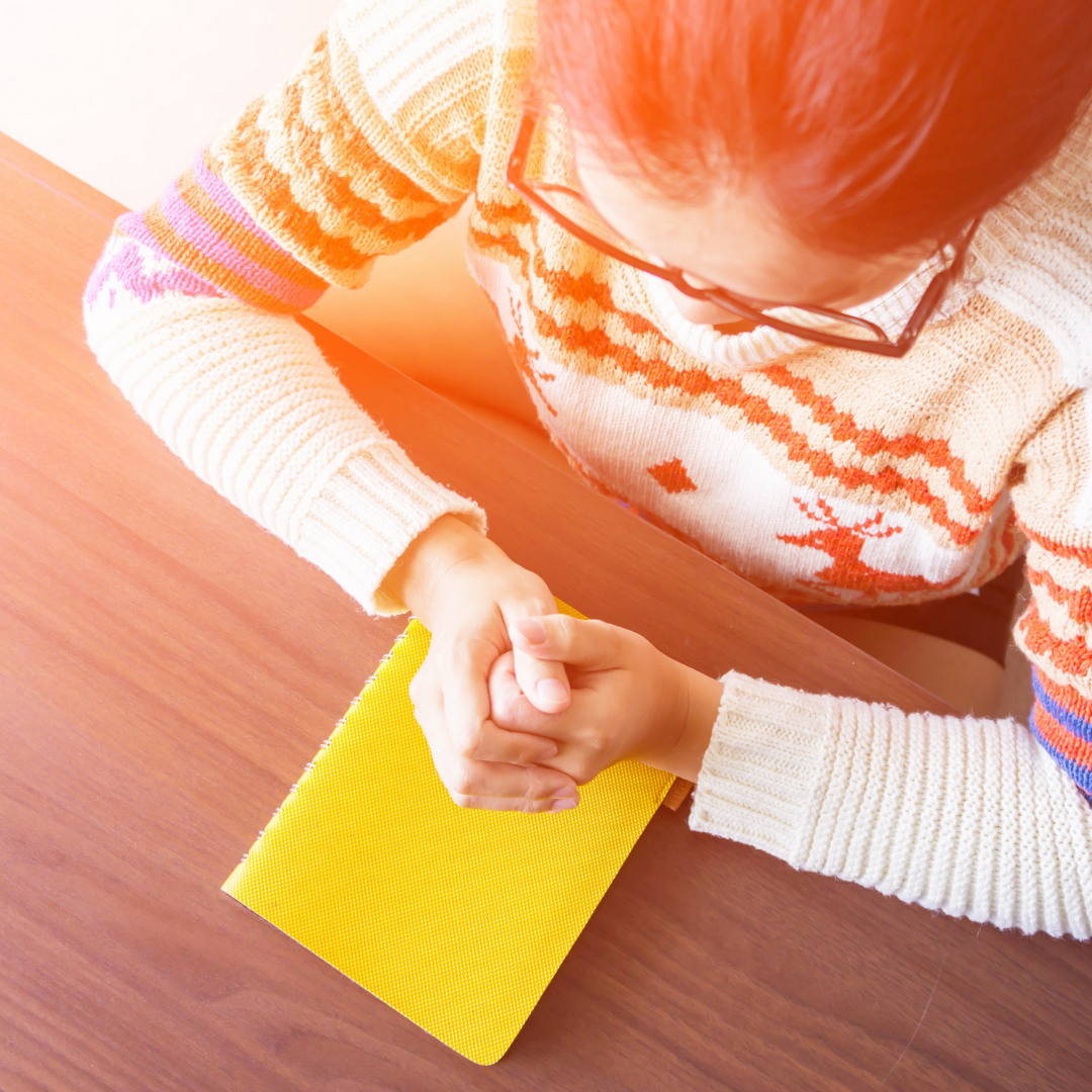 woman praying at a table with yellow prayer book