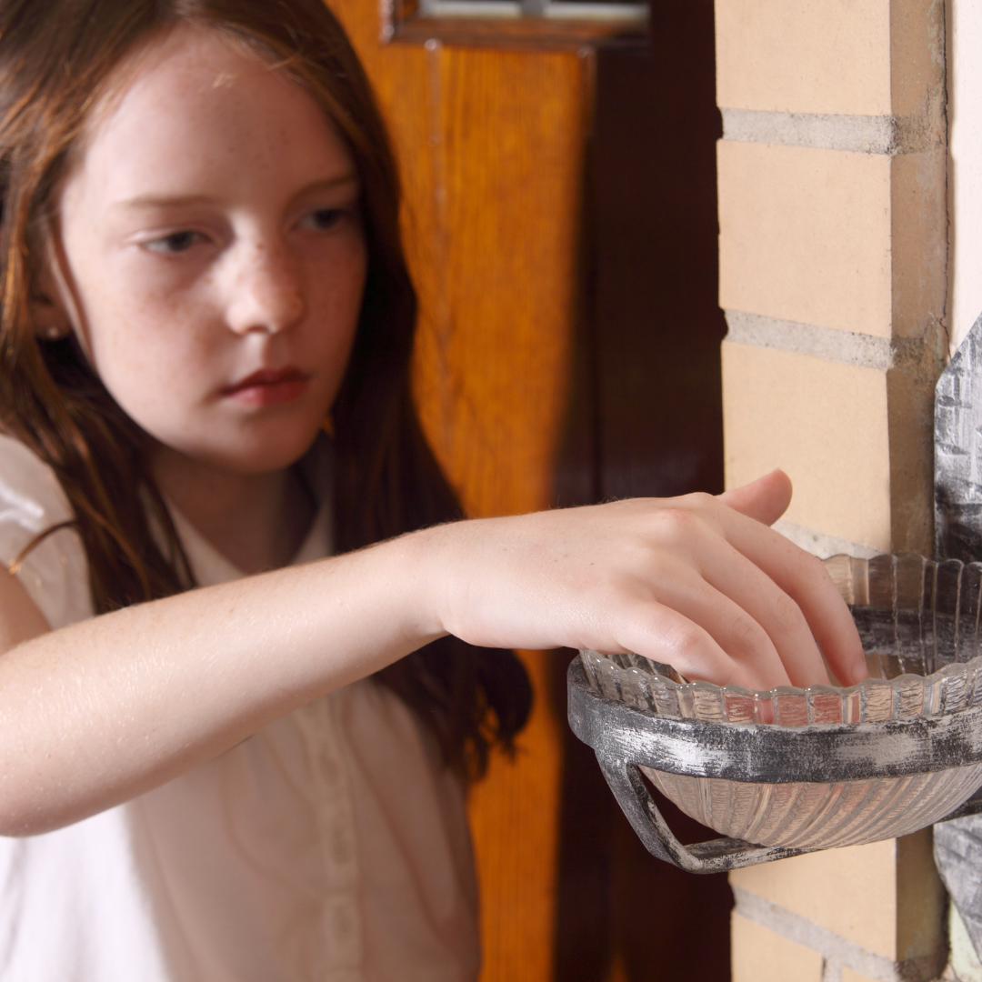 girl dipping her fingers into holy water font next to a door