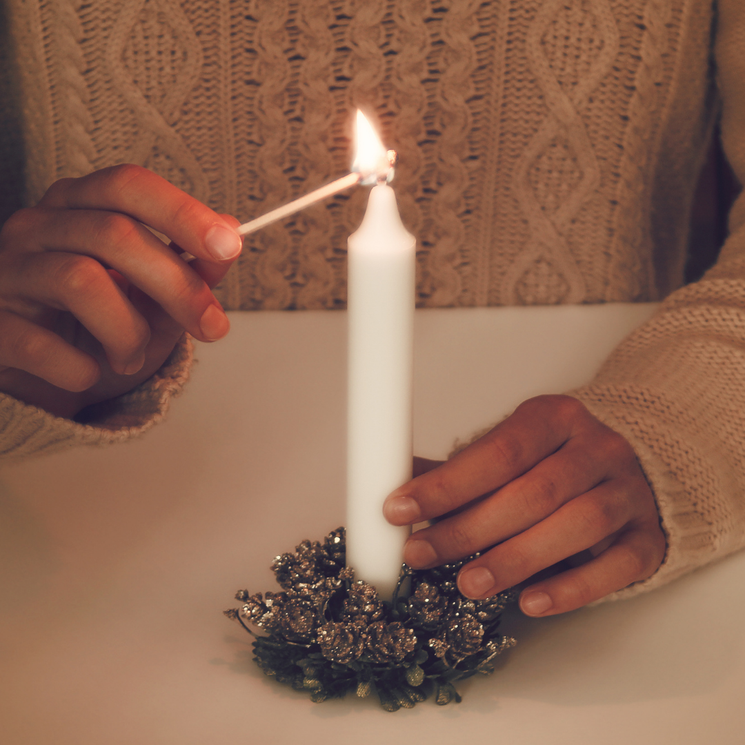 lighting a white candle in a tiny wreath