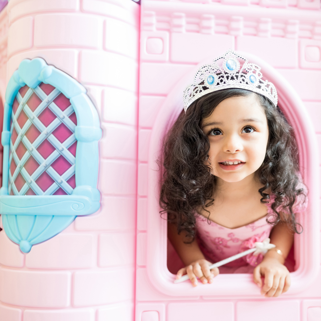 little girl with wand and tiara looking out of pink plastic castle