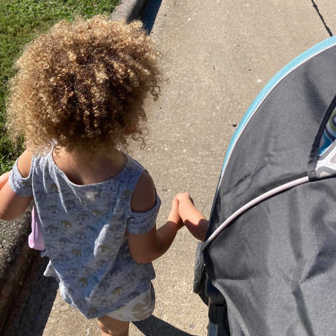toddler holding hands with baby in a stroller