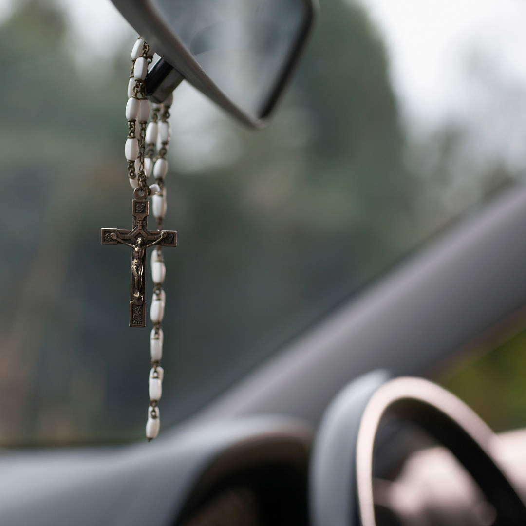 white rosary dangling from rear-view mirror