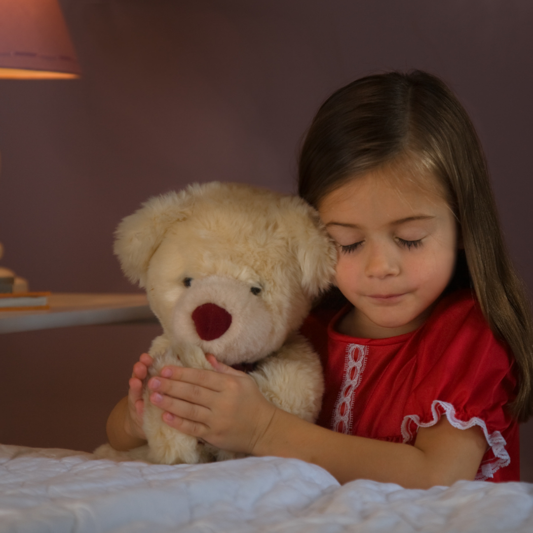 little girl holding teddy bear and praying before bed
