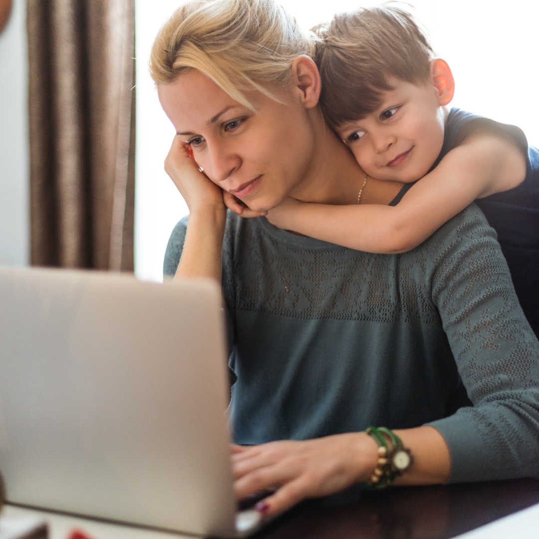 child hugging mom while she works at a computer