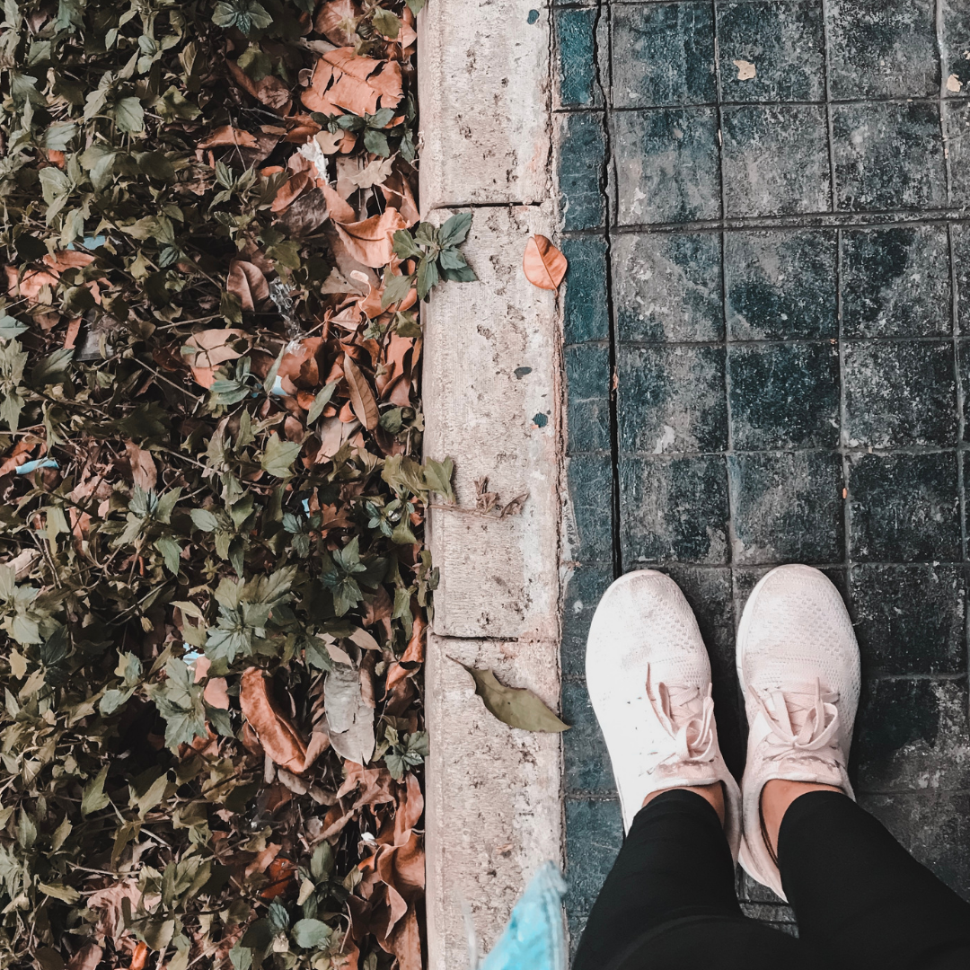 woman in sneakers standing near pile of fallen leaves