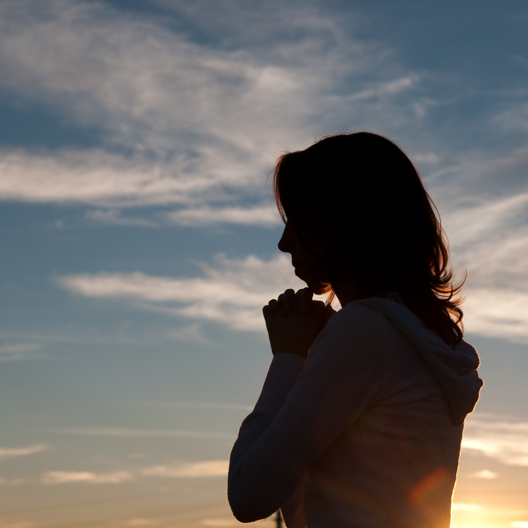 woman praying outdoors, silhouetted against a cloudy sky