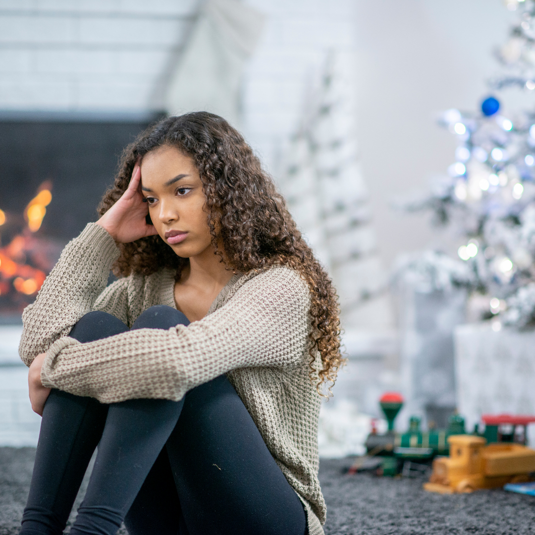 sad woman in front of Christmas tree and fireplace