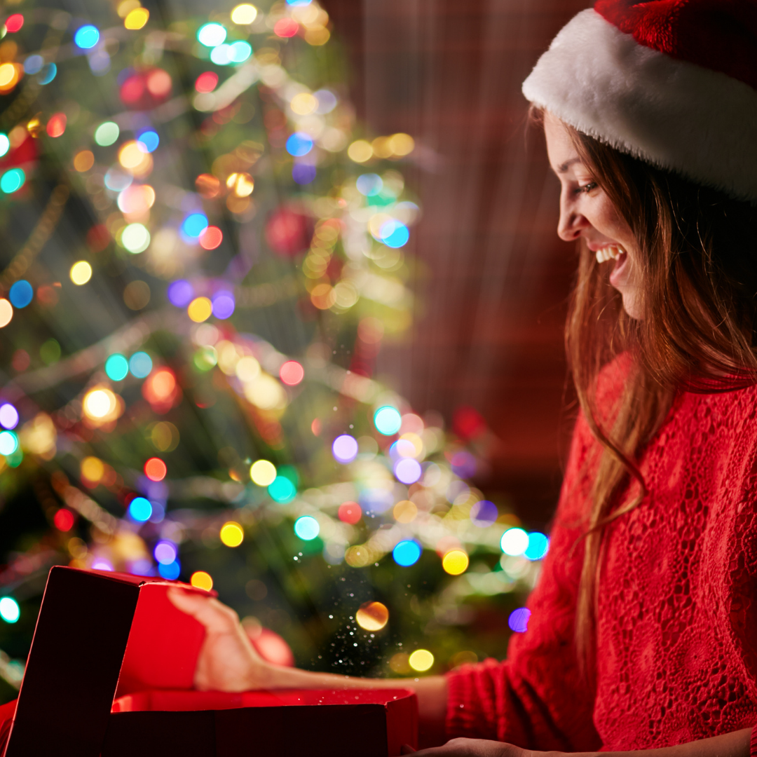 woman wearing santa hat and opening gift next to Christmas tree