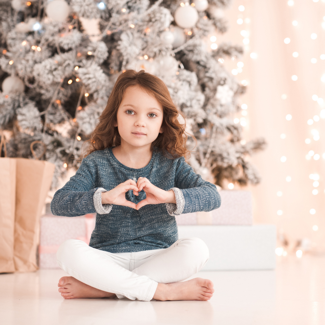 child in front of Christmas tree holding her hands up in the shape of a heart
