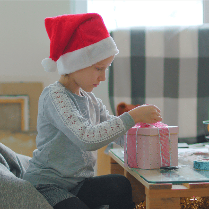 little girl in Santa hat wrapping presents