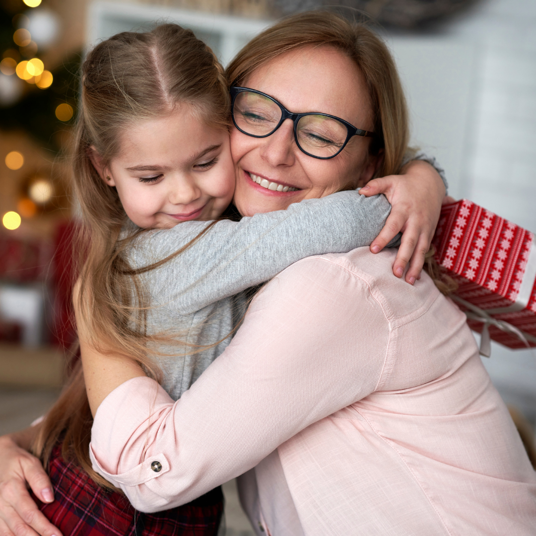 little girl holding Christmas gift and hugging her mom