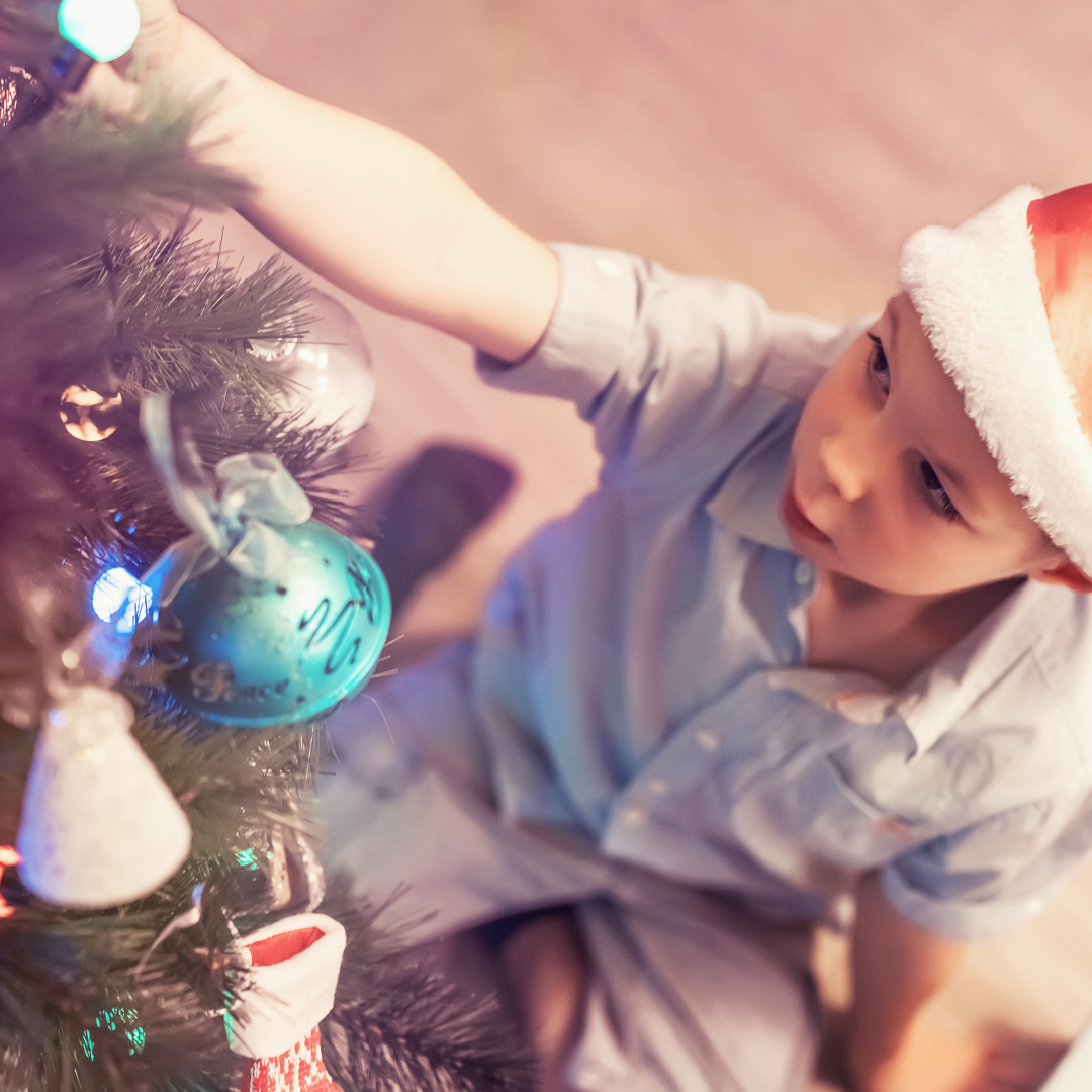 little boy hanging ornaments on a Christmas tree