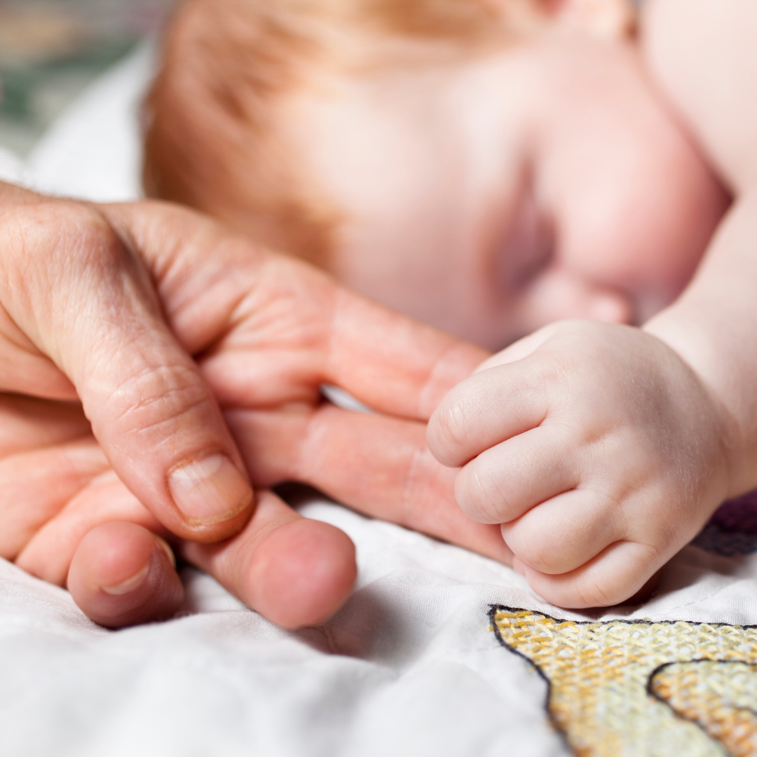 baby holding mom's finger while sleeping