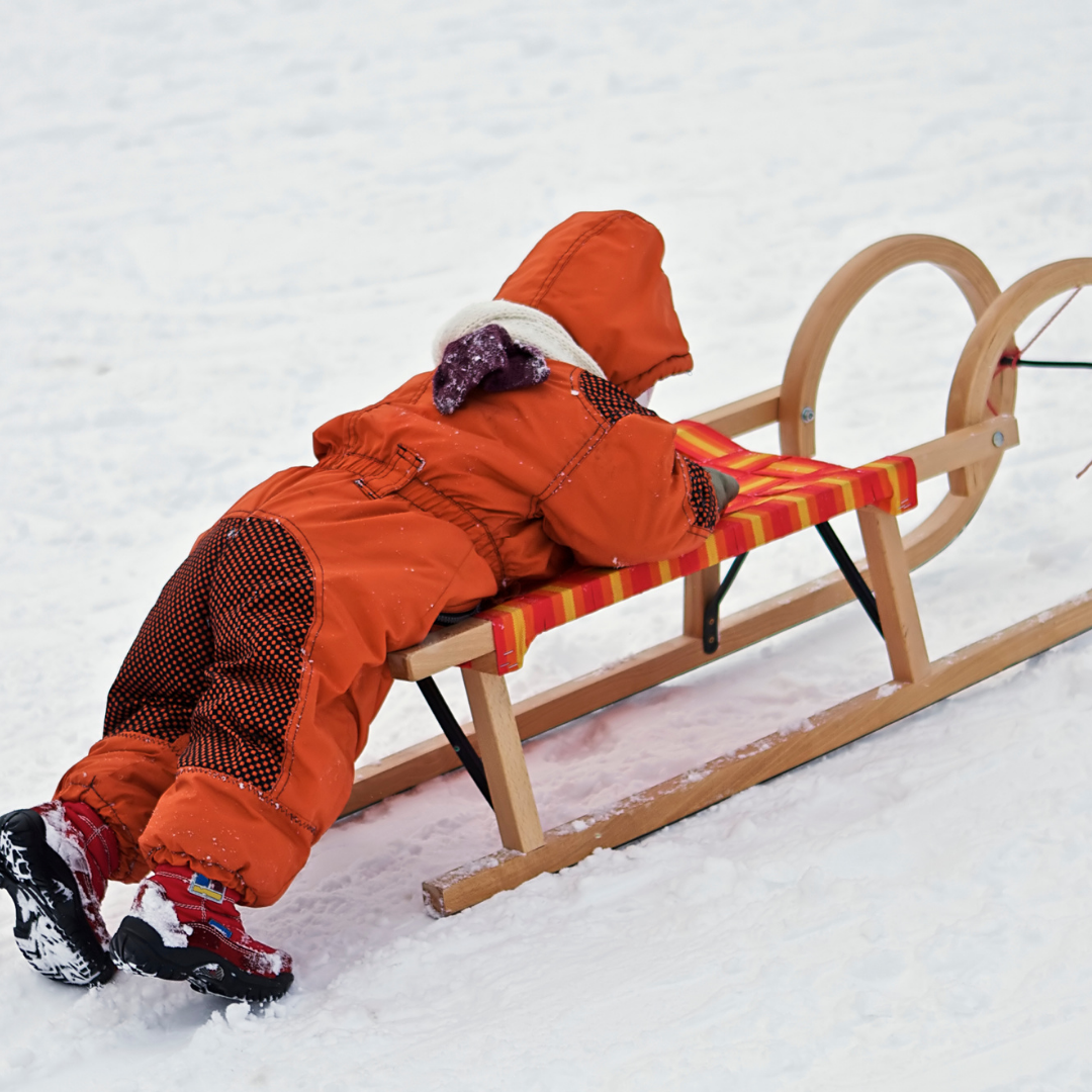 child in red snowsuit on a sled