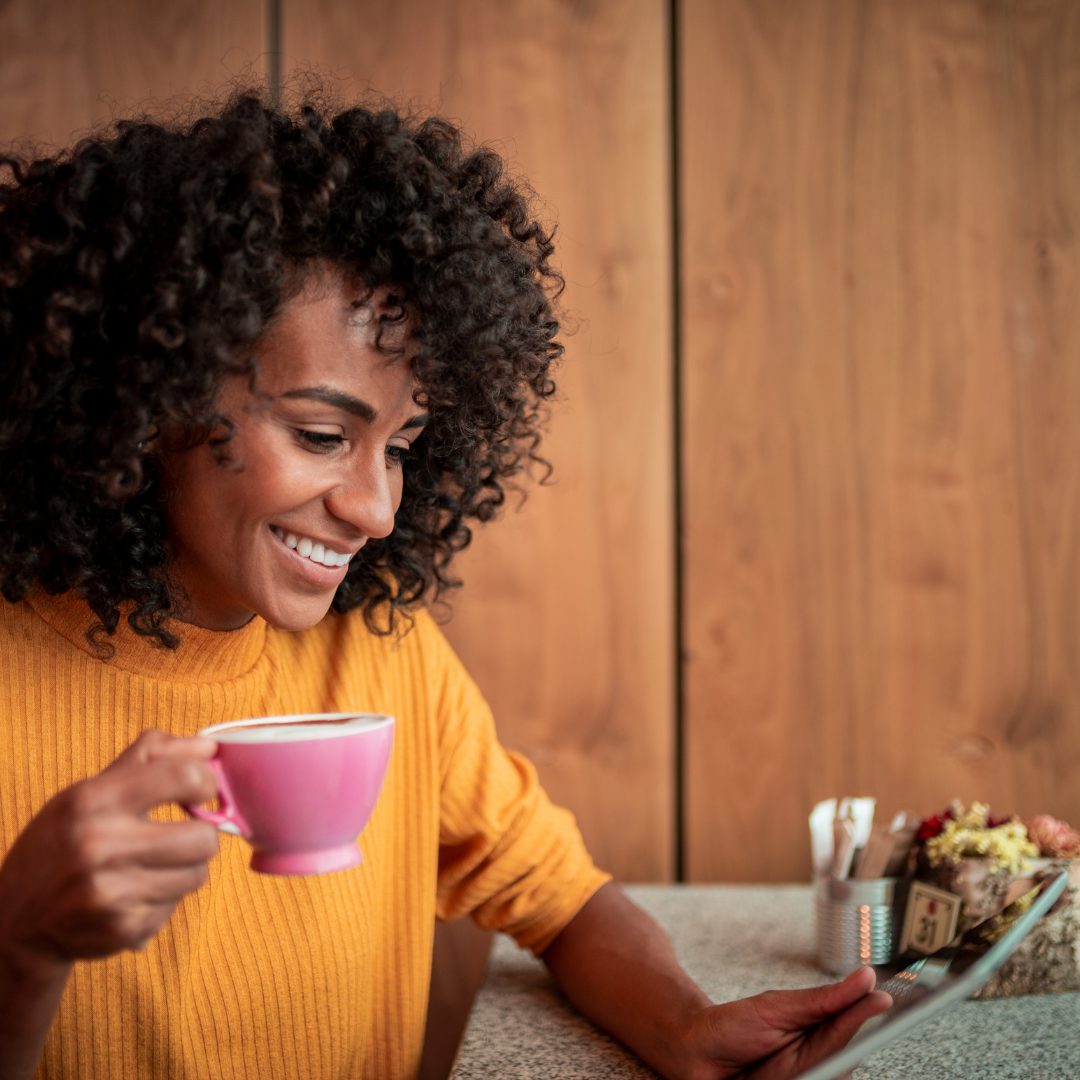 woman drinking coffee and reading on a tablet
