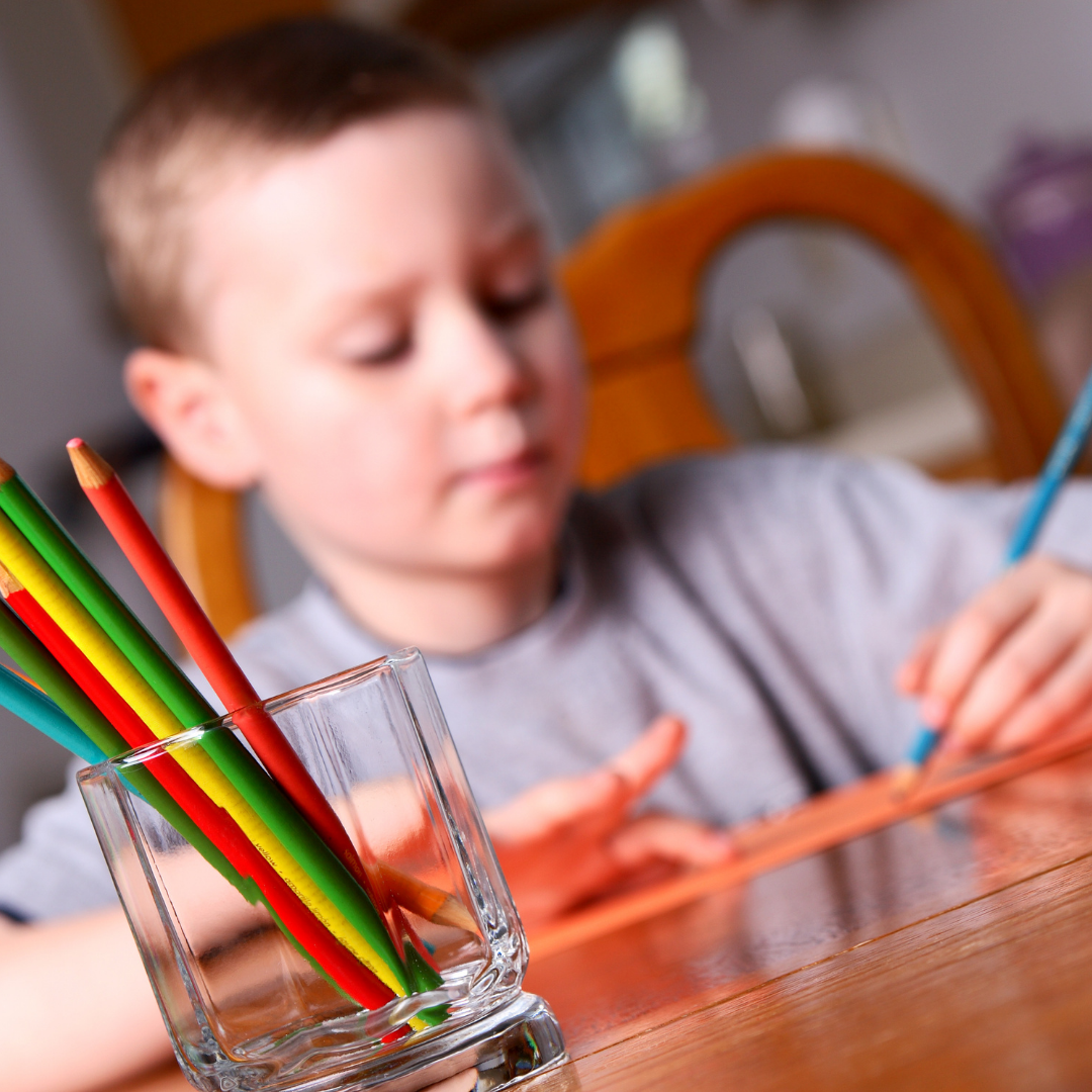 young boy writing with colored pencils