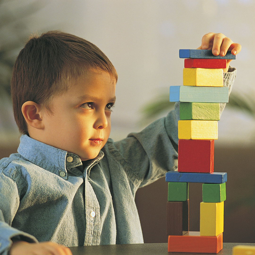 little boy building a tower with colorful wooden blocks