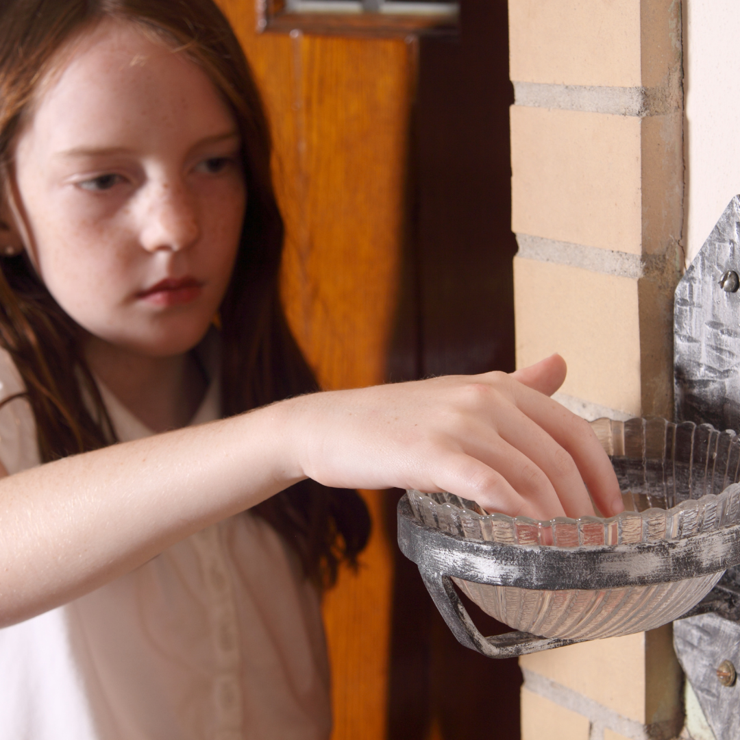 girl dipping fingers into holy water font