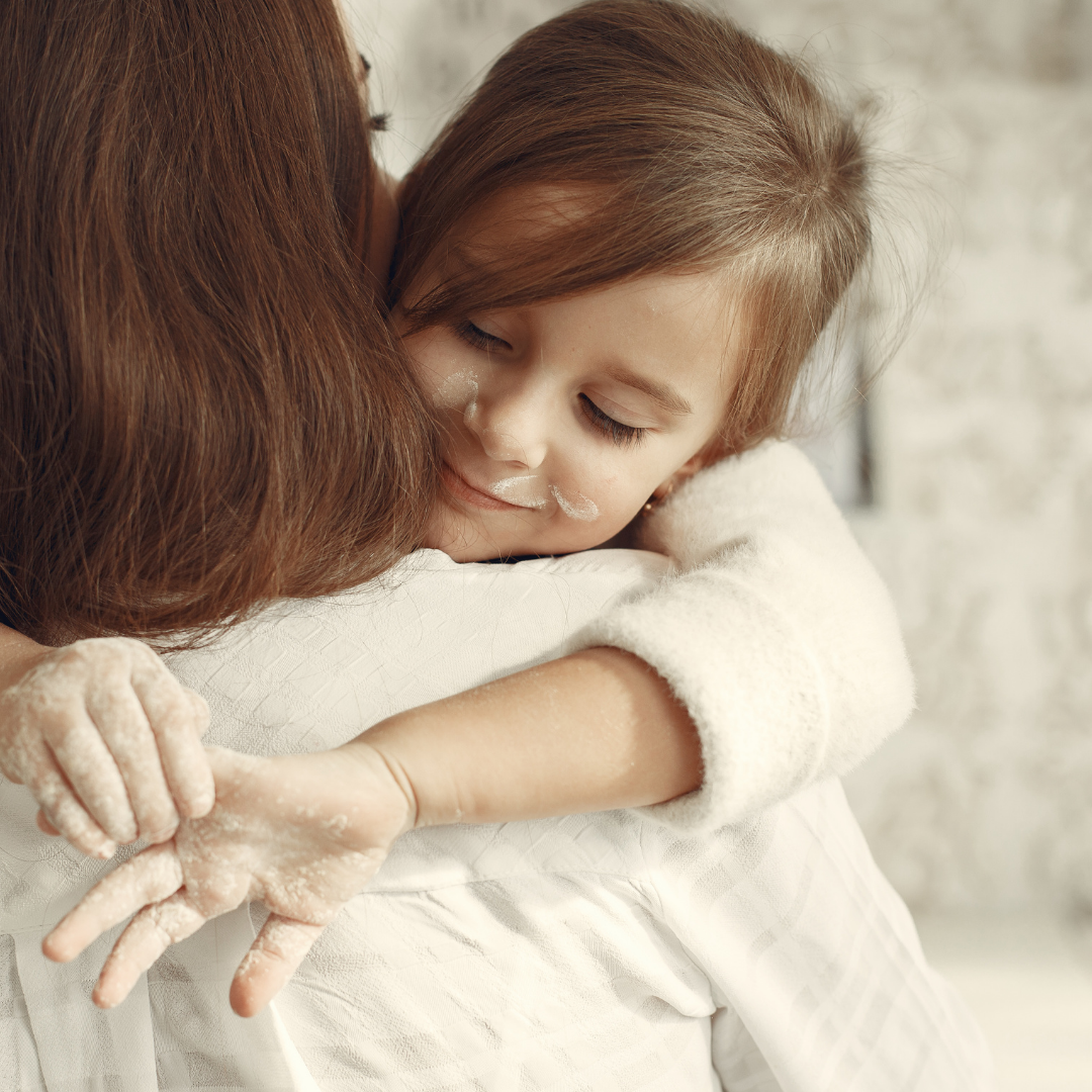 little girl covered in flour and hugging mom