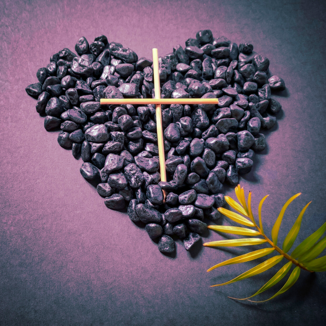 heart made of pebbles with wooden cross and palm front on purple background