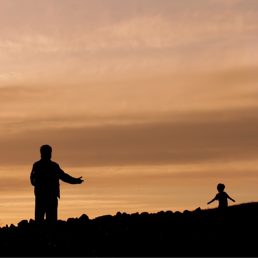 small child running with outstretched arms toward adult at sunset