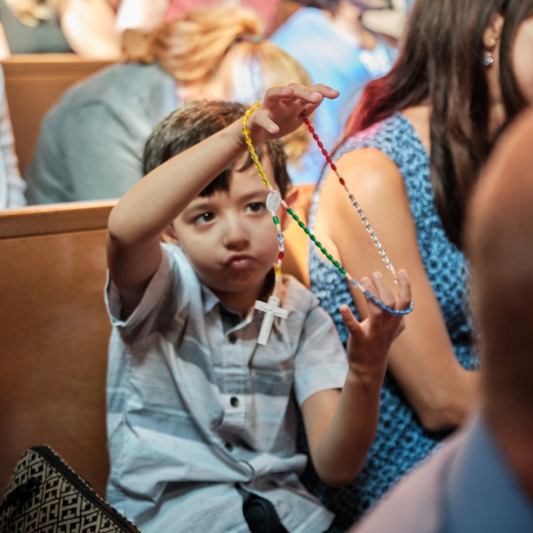 little boy playing with rosary in church pew