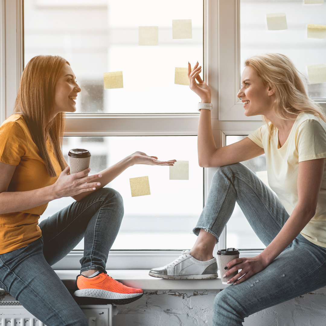 2 women sitting on a windowsill talking and smiling