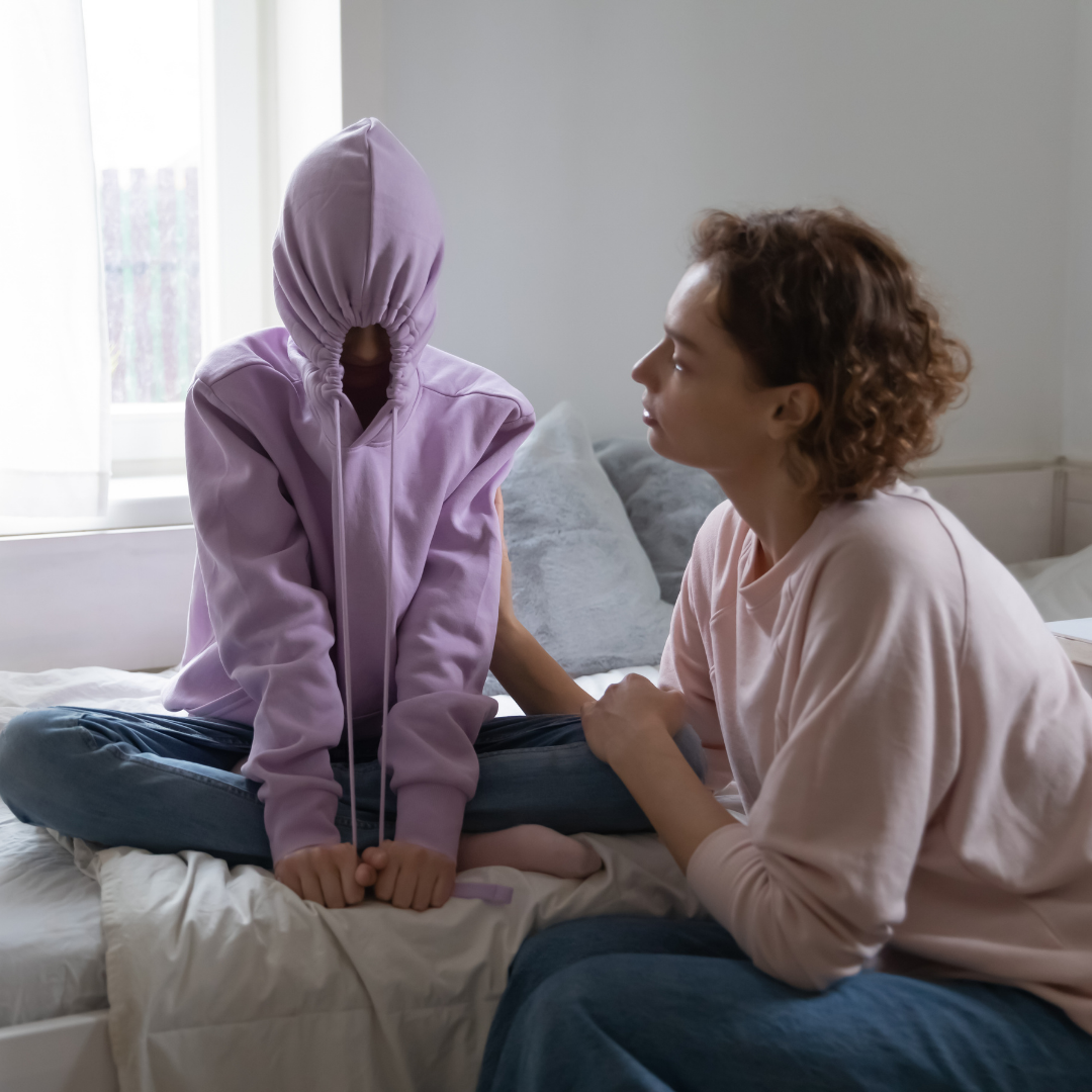 mom talking to teenager who is hiding under a hoodie