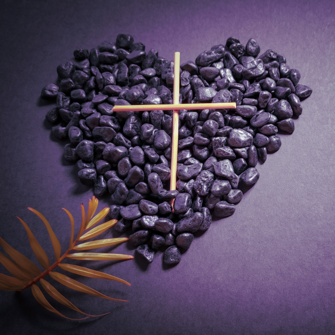 heart shaped of purple stones, with palm frond and small wooden cross