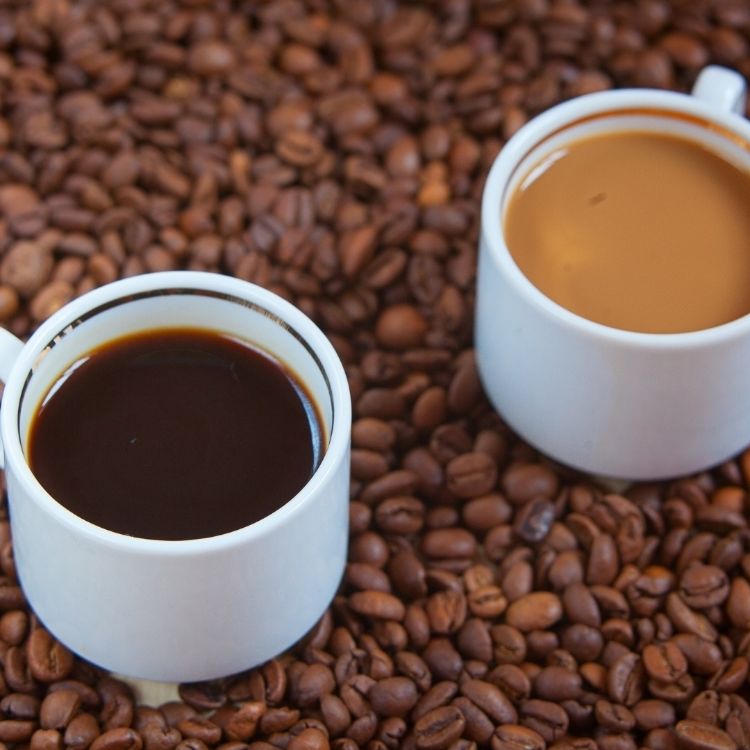 black coffee and coffee with cream sitting in a bed of coffee beans