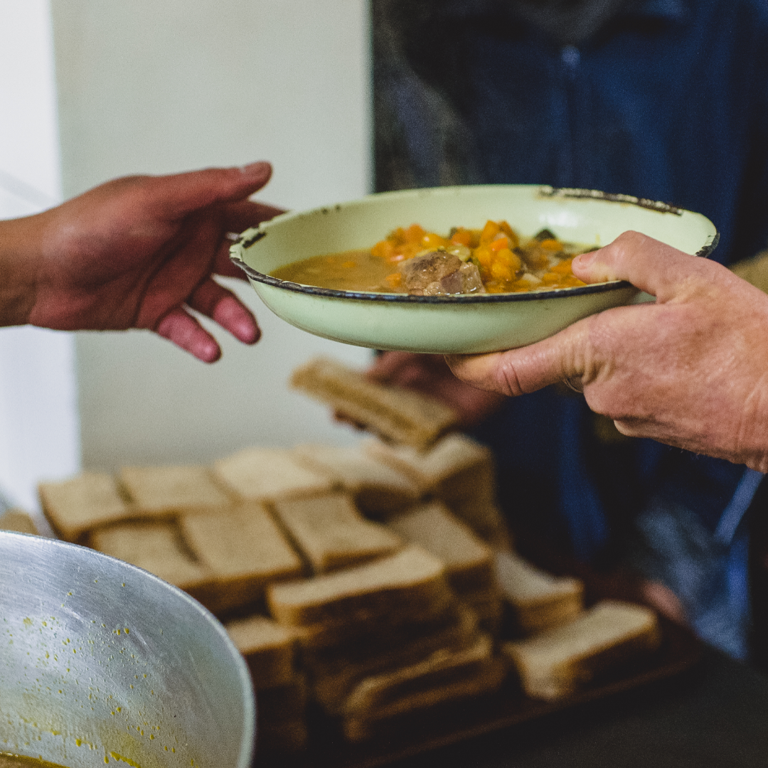 soup kitchen volunteer handing bowl of stew to guest