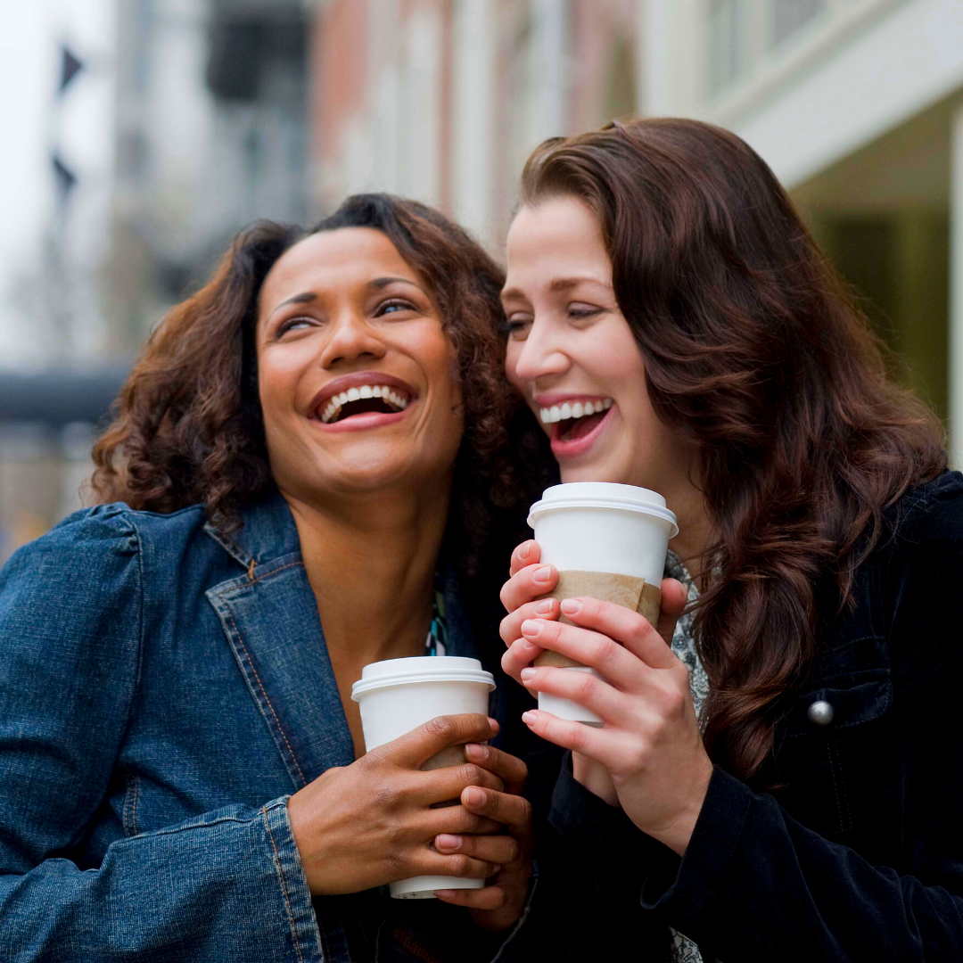 women laughing and holding cups of coffee
