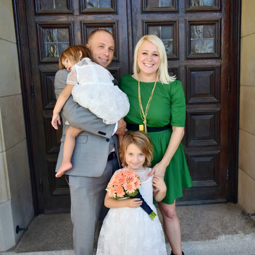 parents with sleeping child at doors of a church, with another child in front of them