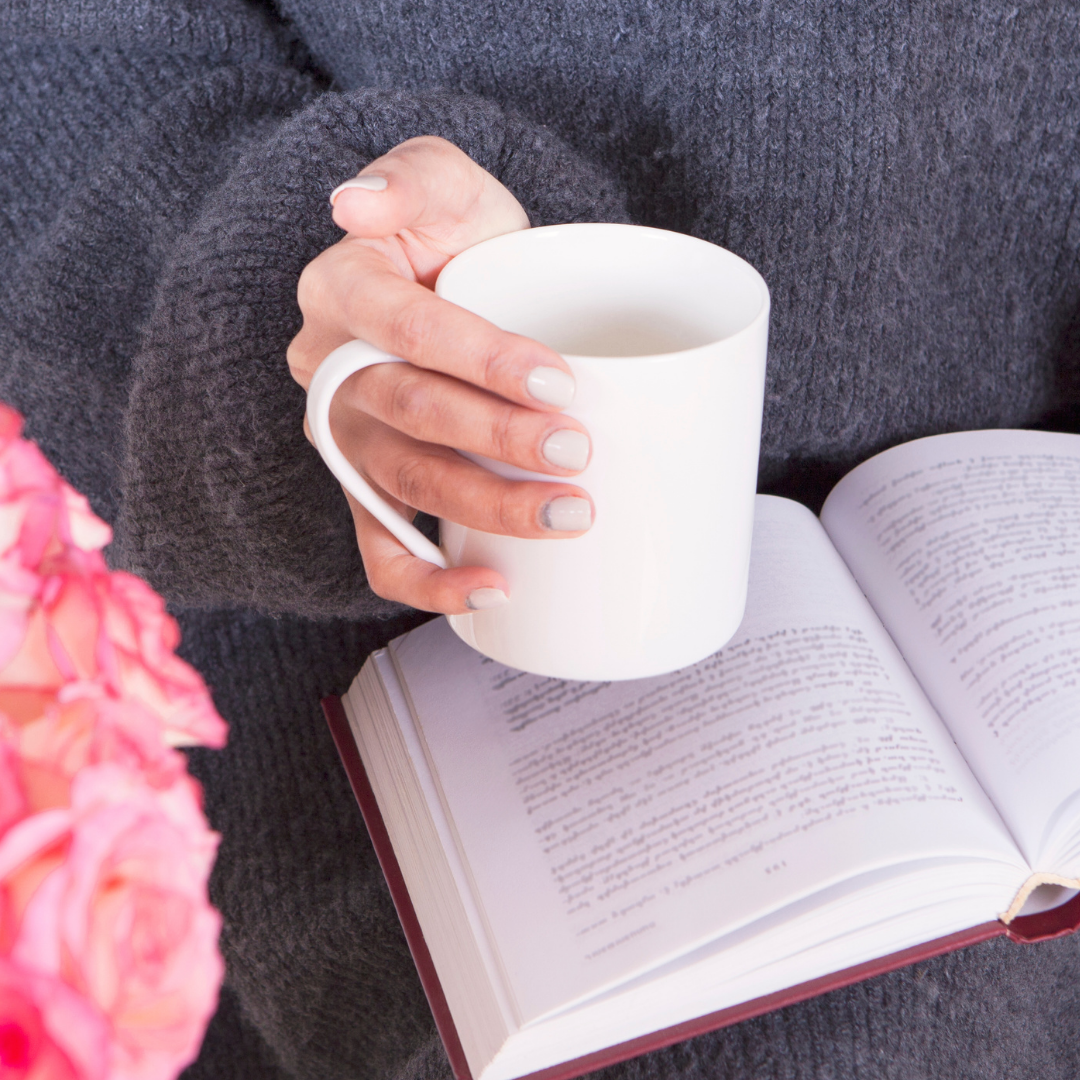 reading a book with coffee cup, next to pink flowers