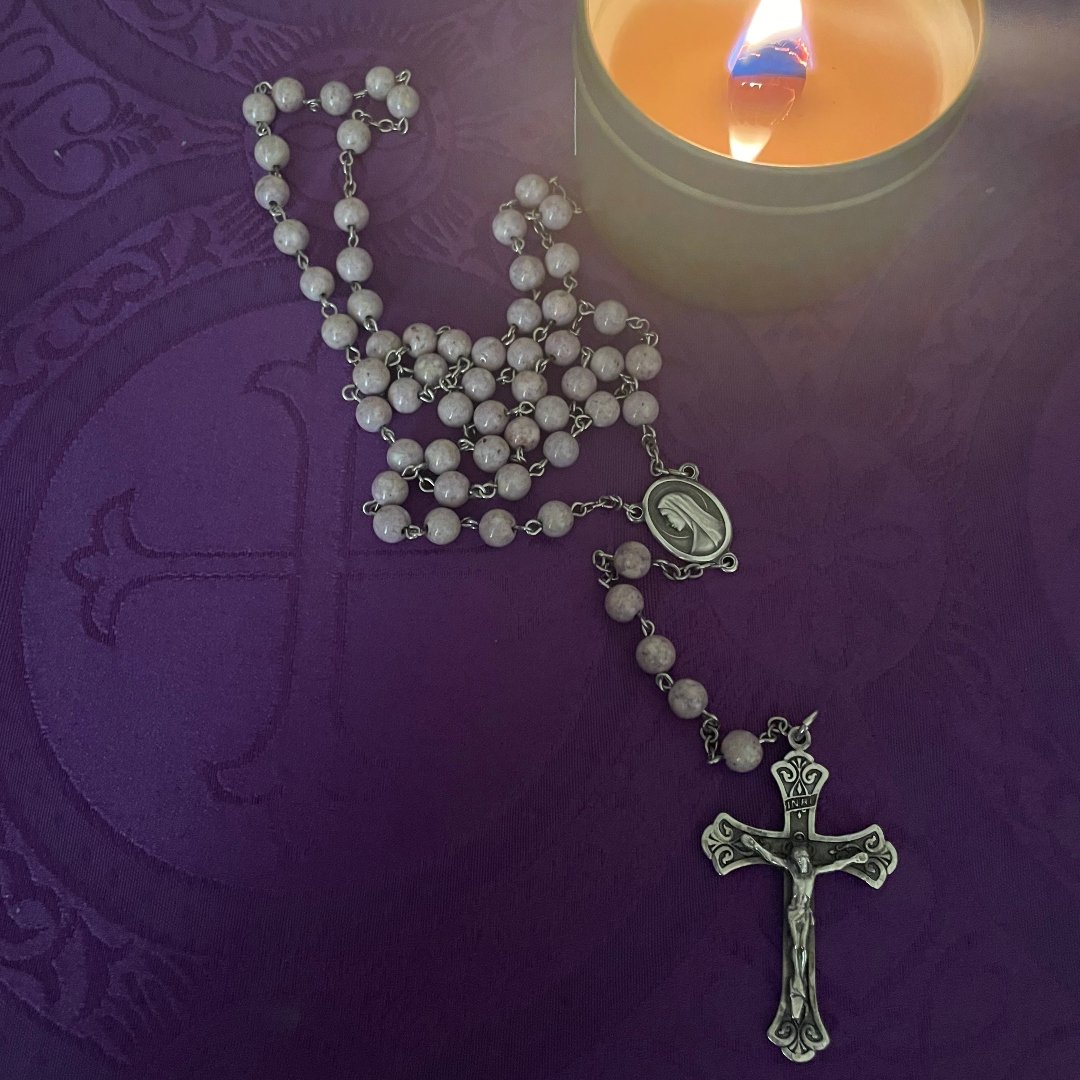 rosary and lit candle on a prayer table
