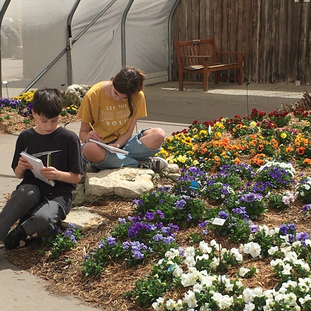 2 teens drawing next to flower garden