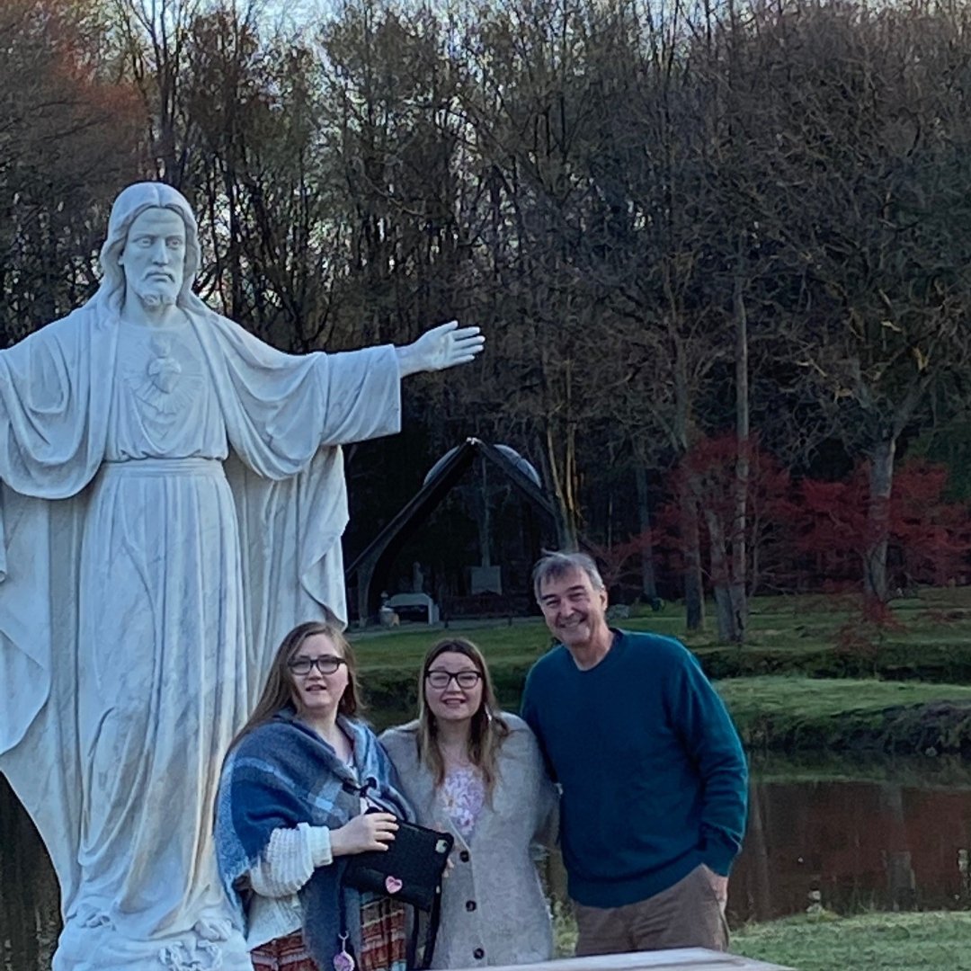 two young women and their dad next to statue of Risen Christ