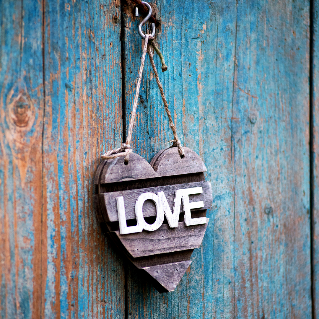 heart with word "love" hanging against a blue wooden fence