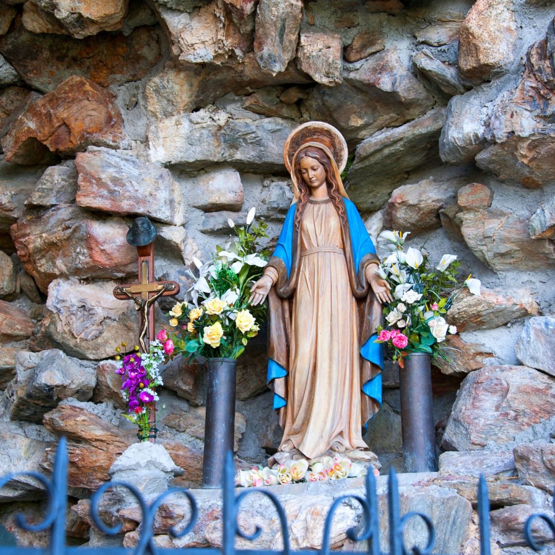 statue of Mary surrounded by crucifix and flowers, in a grotto