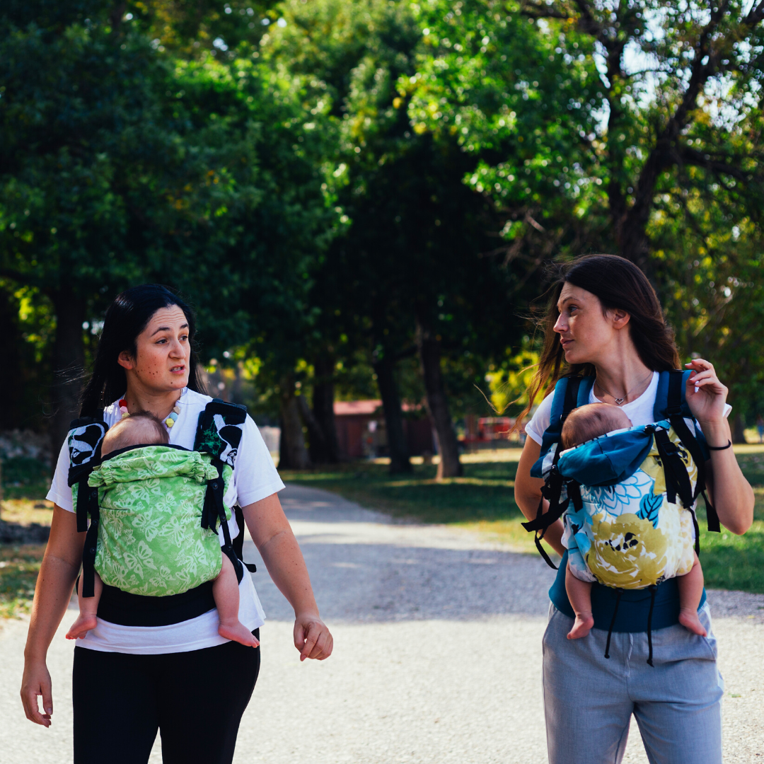 2 women talking as they walk with babies in carriers