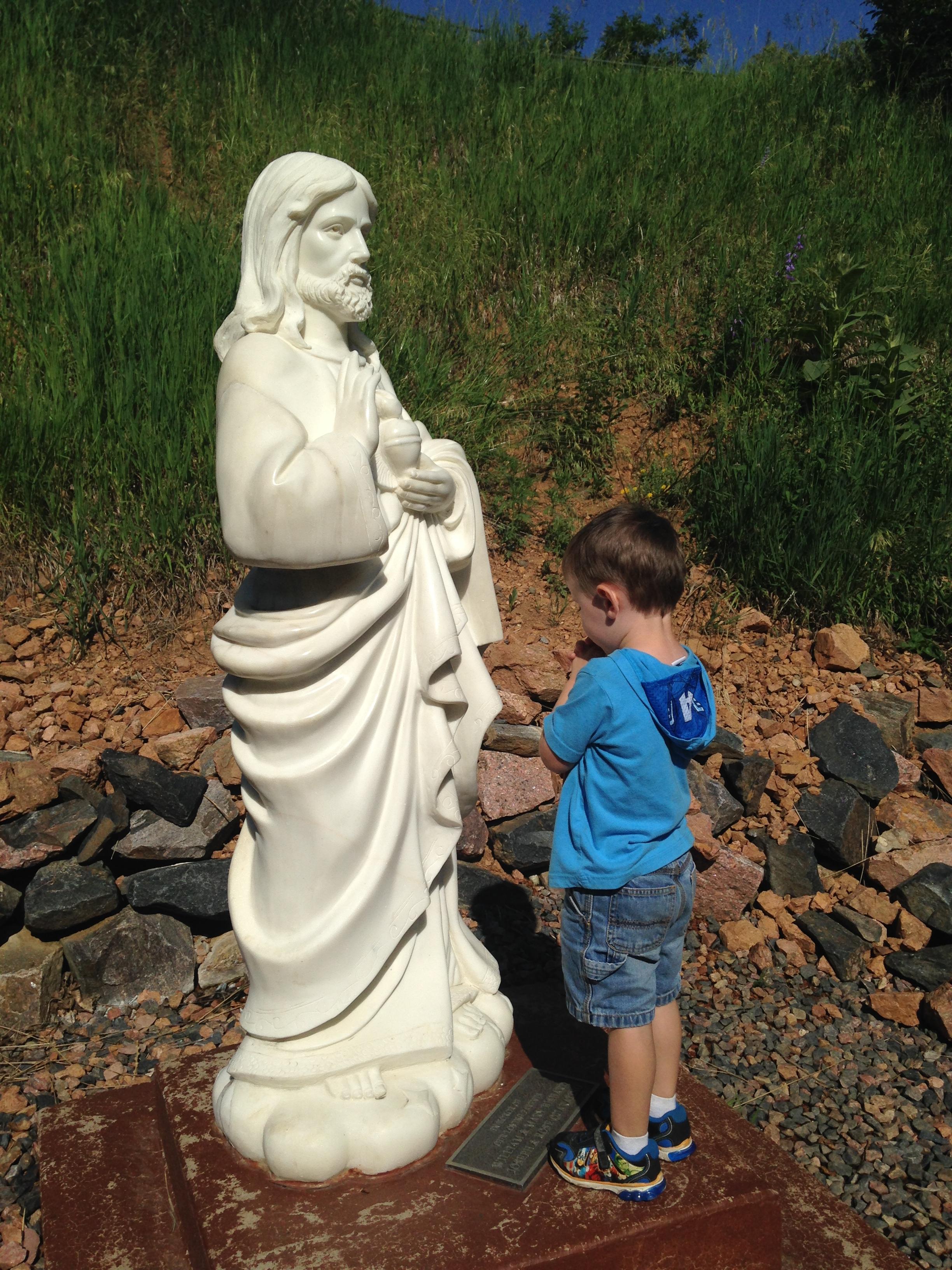 little boy praying in front of Sacred Heart statue at Cabrini Shrine