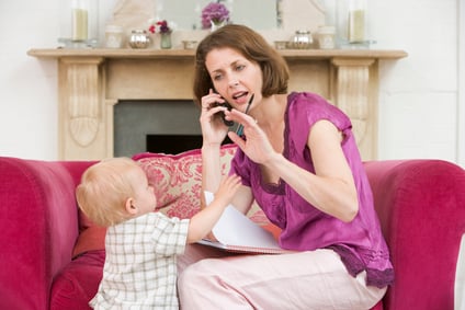Mother using telephone in living room with baby frowning