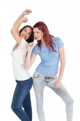 Two cheerful young female friends dancing over white background
