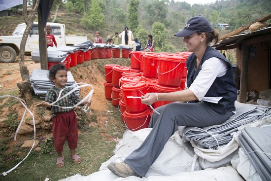 More than 100,00 homes were destroyed in the earthquake upending life for families in both urban Kathmandu and remote mountain communities.  CRS staff Elizabeth Tromans is here distributing relief supplies to families in Gorkha district, demonstrating for a child how the ties are used to secure the tarps her team is distributing. Photo by Jennifer Ryan/CRS