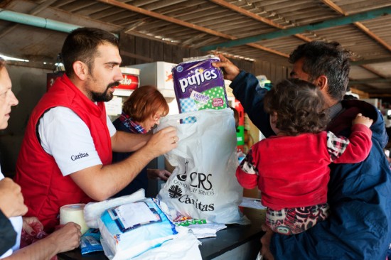 Caritas volunteer, Seka Maksimovic, hands our rolls of toilet paper to refugees at Belgrade, Serbia's Mixer House. CRS, working with Caritas, organized a distribution center providing hygiene kits containing soap, shampoo, sanitary napkins, toothbrushes, toothpaste, diapers, clothing for infants and other basic supplies to the thousands of refugees traveling to Germany. 